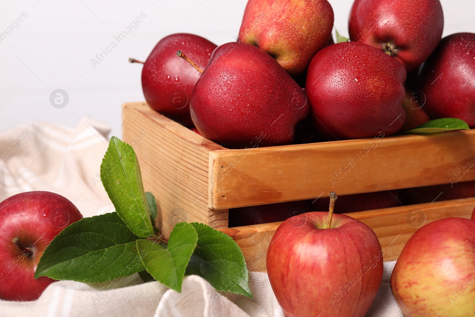 Photo of Fresh red apples and leaves in wooden crate on table, closeup