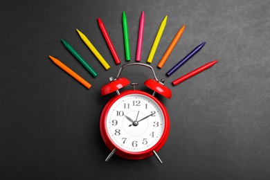 Photo of Alarm clock and colorful pencils on blackboard, flat lay. School time