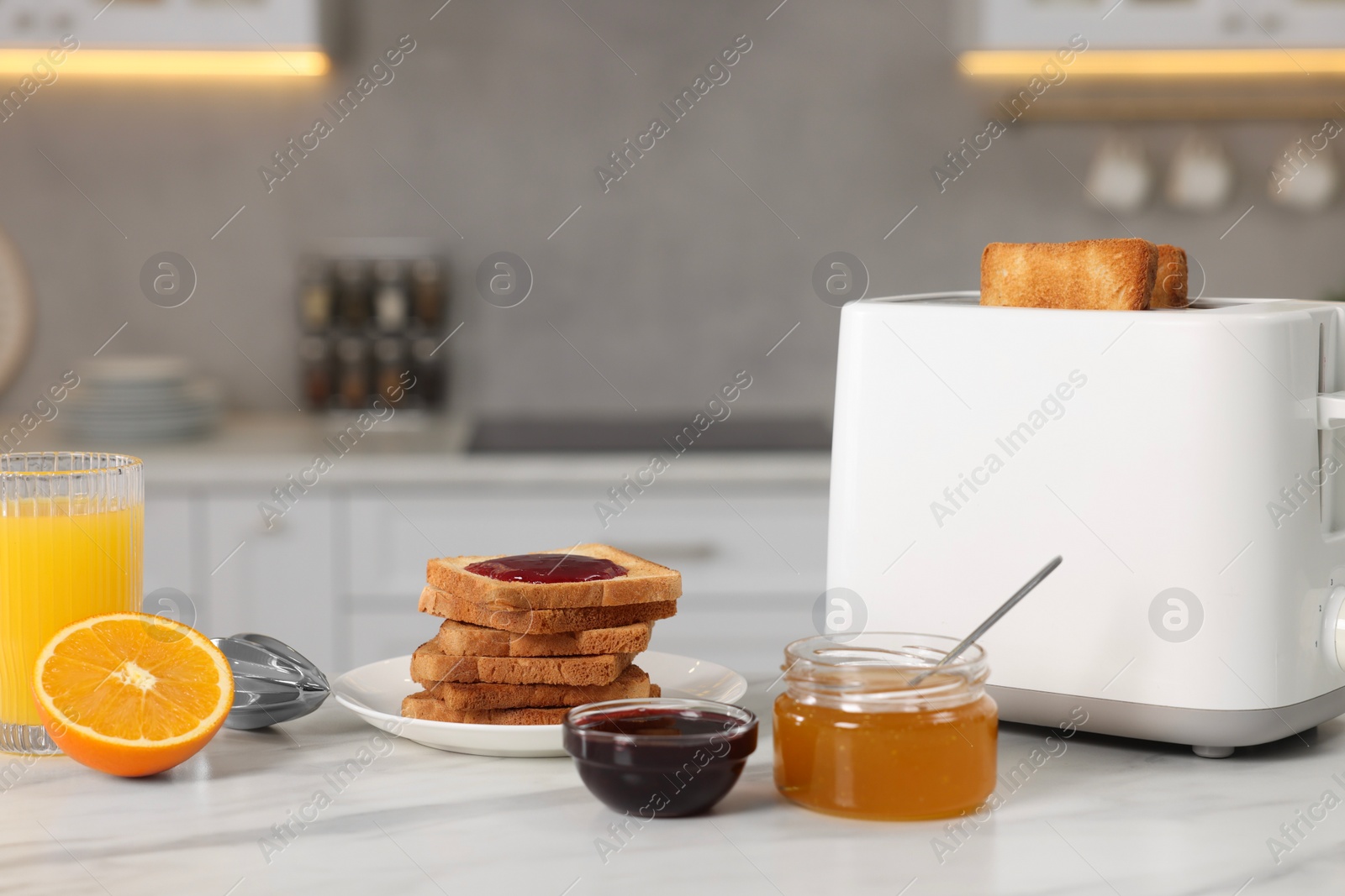 Photo of Making toasts for breakfast. Appliance, crunchy bread, honey, jam and orange fresh on white table in kitchen