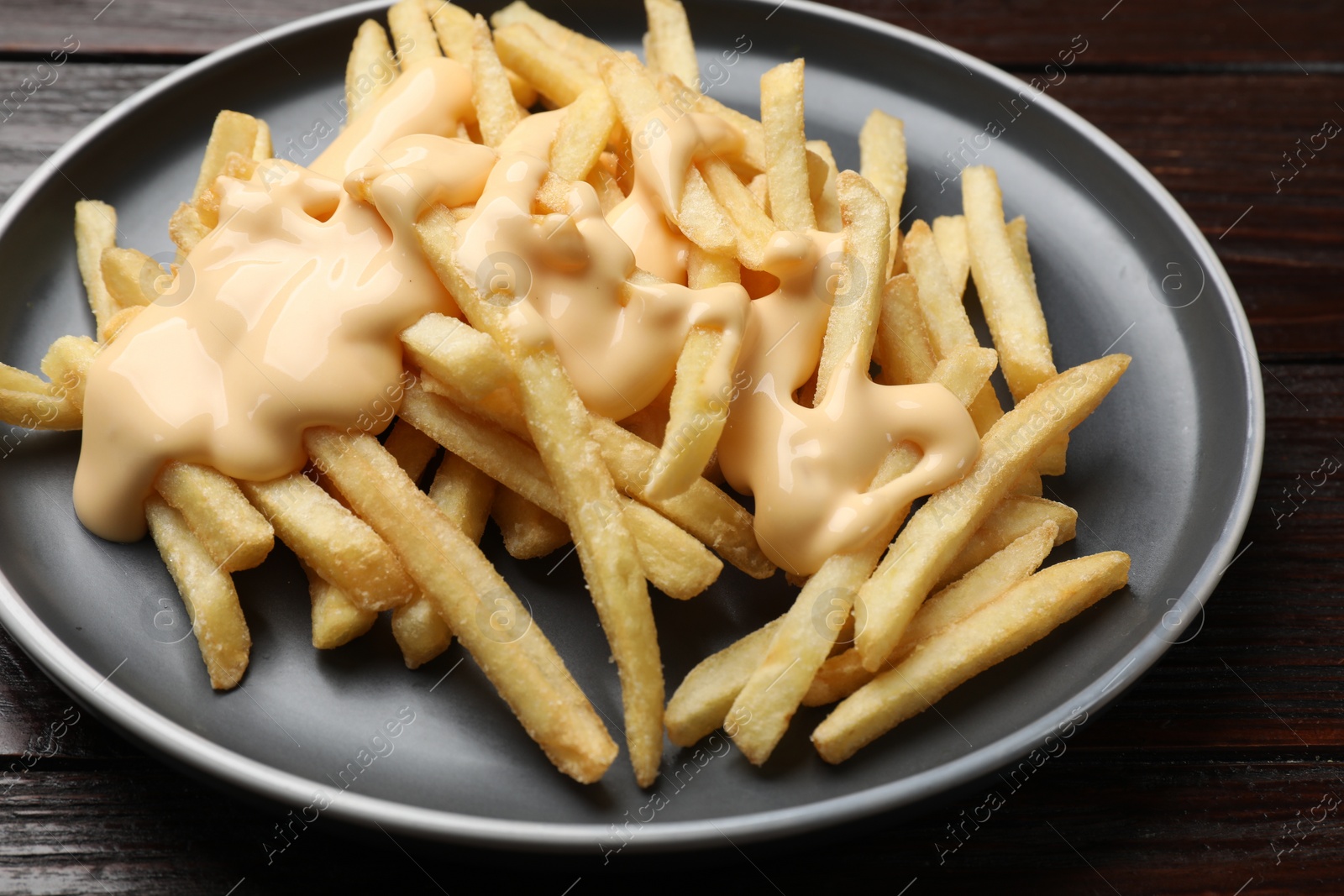 Photo of Delicious french fries with cheese sauce on wooden table, closeup