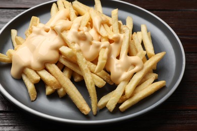 Photo of Delicious french fries with cheese sauce on wooden table, closeup