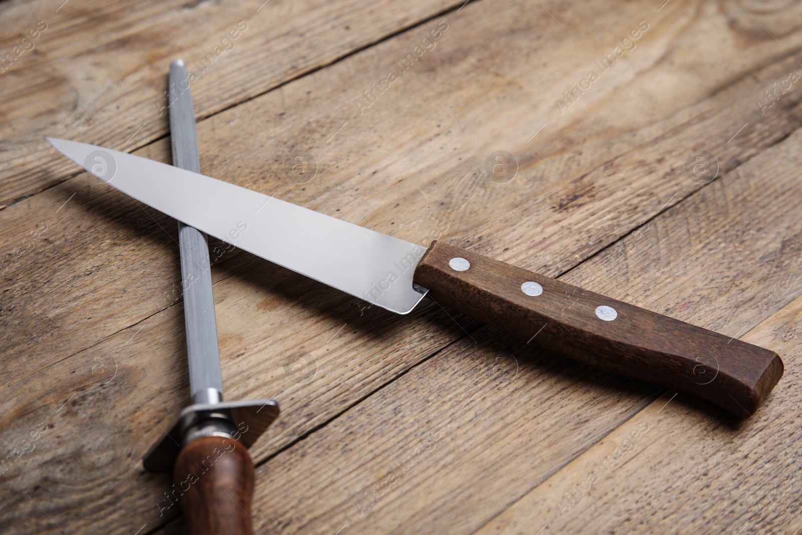 Photo of Sharpening steel and knife on wooden table, closeup