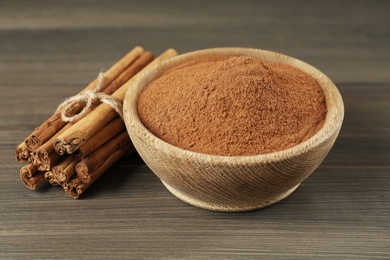 Aromatic cinnamon powder in bowl and sticks on wooden table