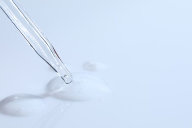 Glass pipette and transparent liquid on white background, closeup. Space for text