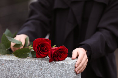Woman with red roses near light grey tombstone outdoors, closeup. Funeral ceremony