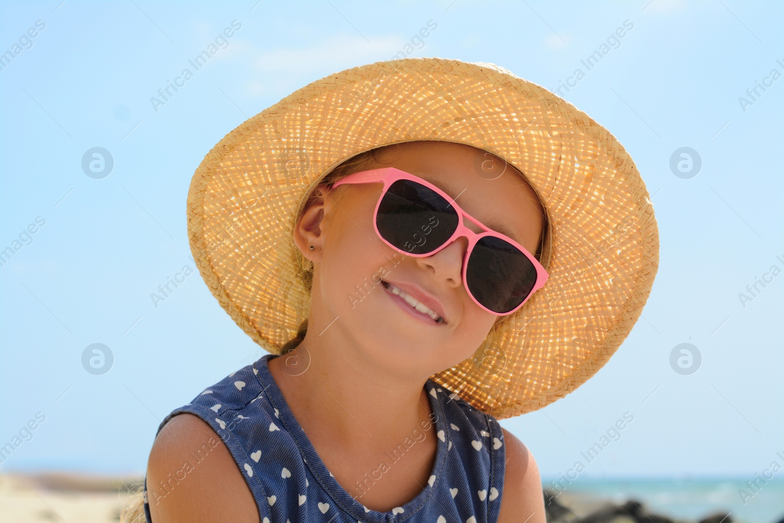 Photo of Little girl wearing sunglasses and hat at beach on sunny day