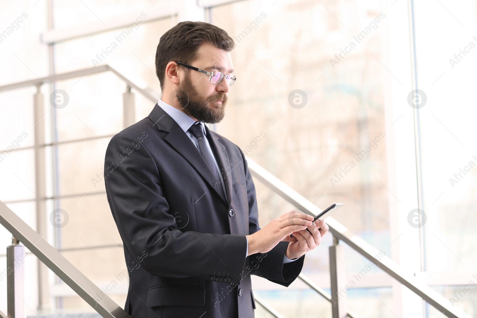 Photo of Portrait of confident mature man with mobile phone in elegant suit on stairs