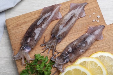 Photo of Fresh raw squids with lemon and parsley on wooden board, top view