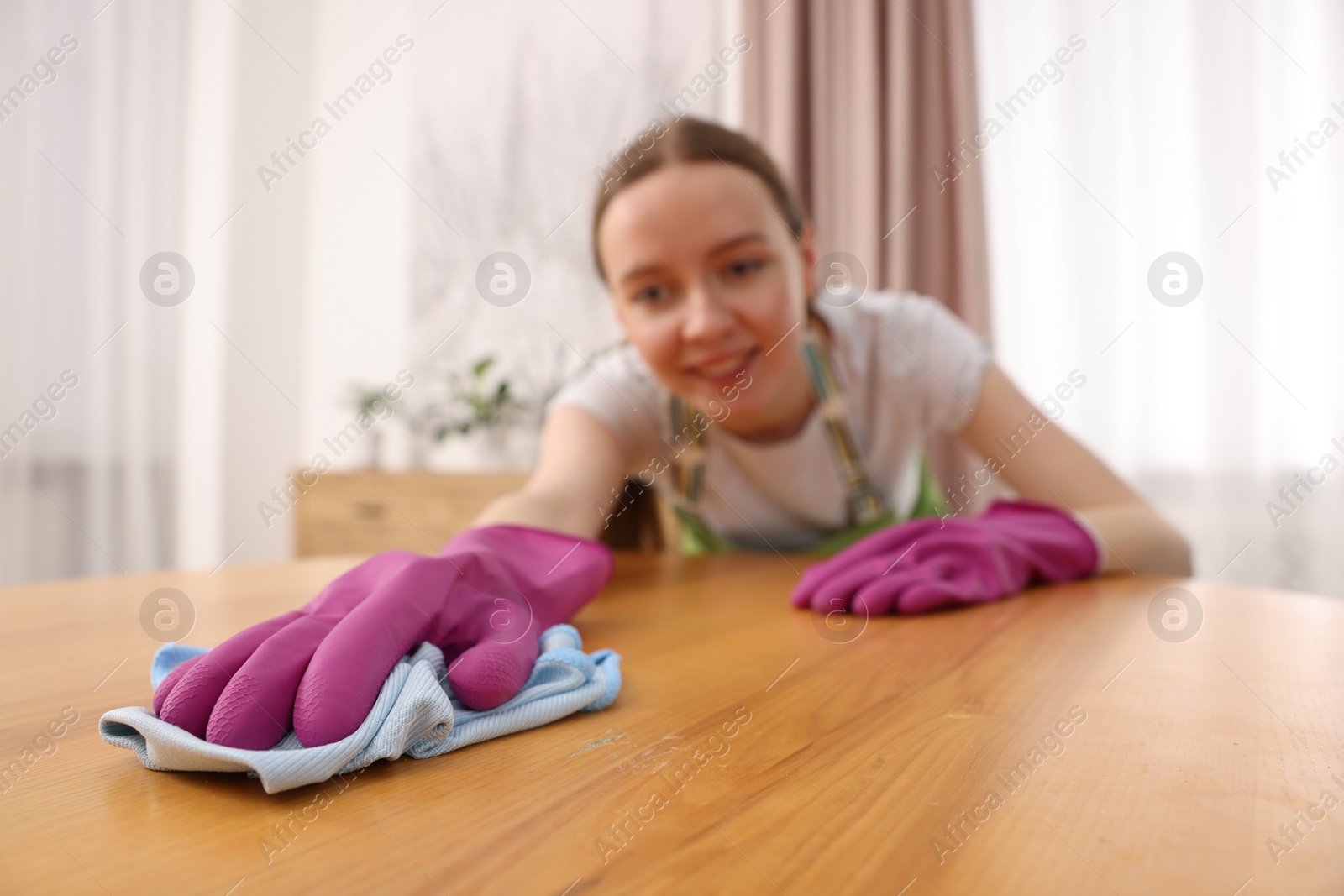 Photo of Woman with microfiber cloth cleaning wooden table in room, selective focus