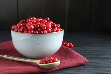 Photo of Cranberries in bowl and spoon on black wooden table, closeup. Space for text