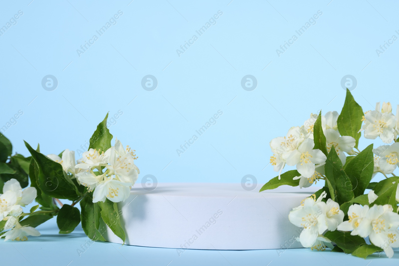 Photo of Presentation of product. White podium and beautiful jasmine flowers on light blue background, space for text