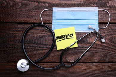 Photo of Note with word Monkeypox, mask and stethoscope on wooden table, flat lay