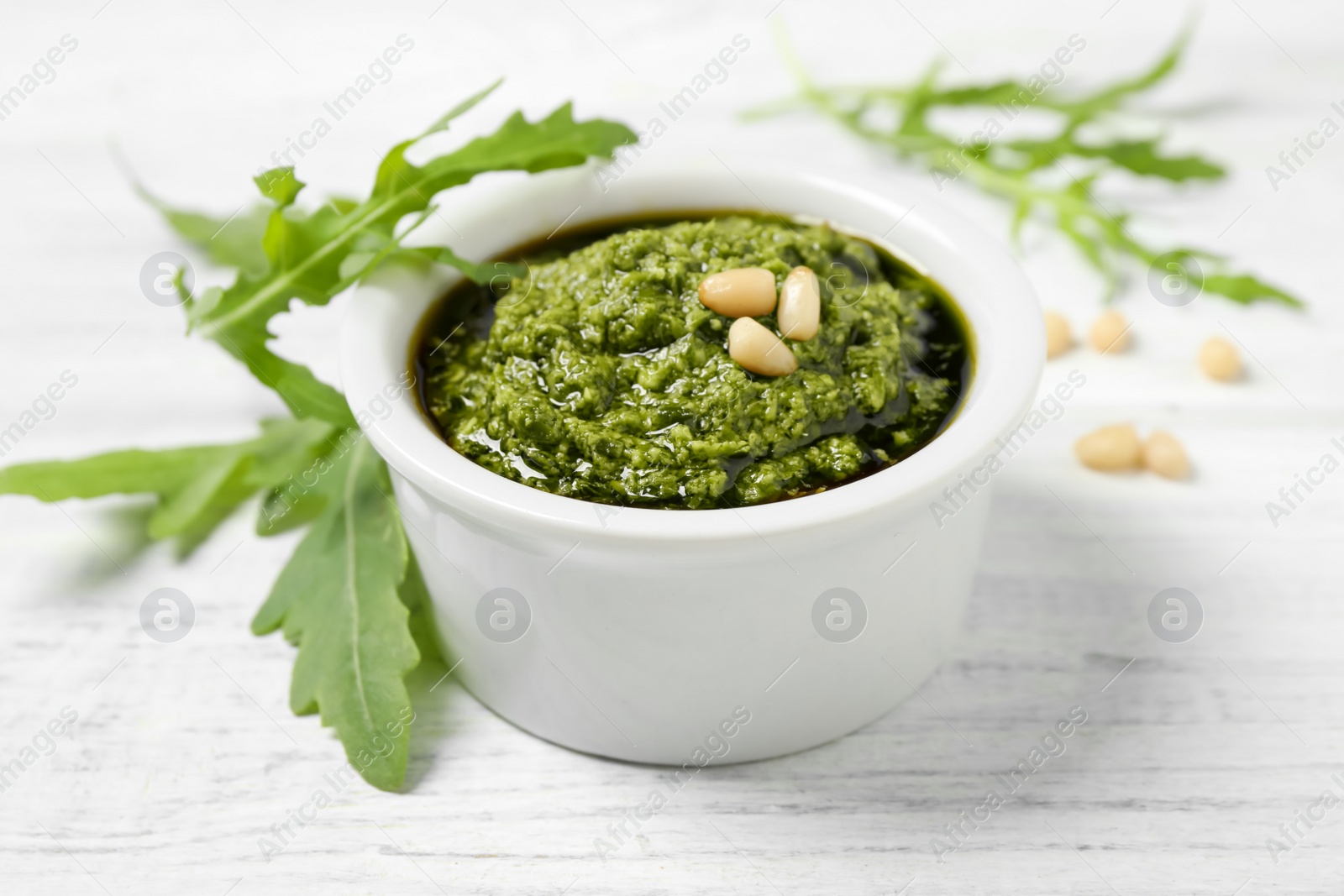 Photo of Bowl of tasty pesto and arugula on white wooden table