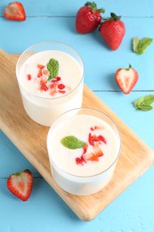 Tasty yogurt in glasses and strawberries on light blue wooden table