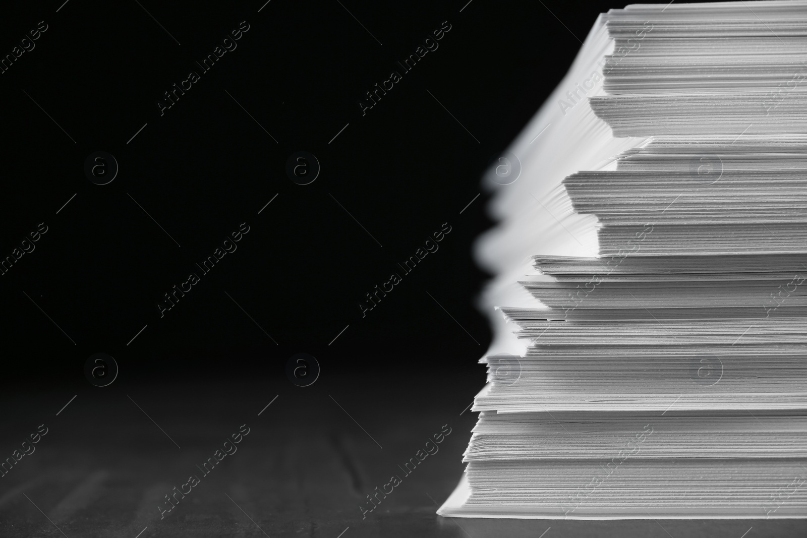 Photo of Stack of blank paper on grey stone table against dark background. Space for text