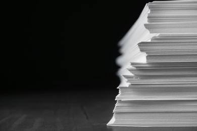 Photo of Stack of blank paper on grey stone table against dark background. Space for text