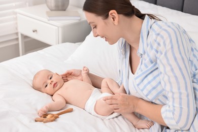 Happy young woman applying body cream onto baby`s skin on bed