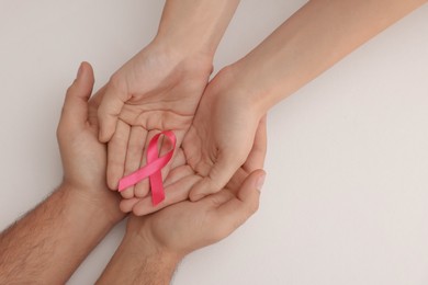 Photo of Couple holding pink ribbon on white background, top view. Breast cancer awareness