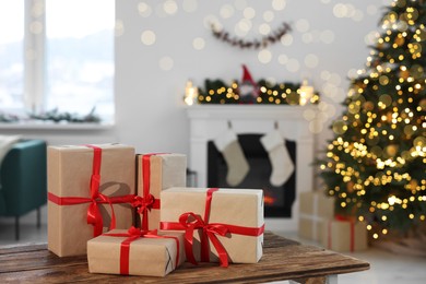 Photo of Many different gift boxes on wooden table against blurred festive lights in living room, space for text. Christmas presents