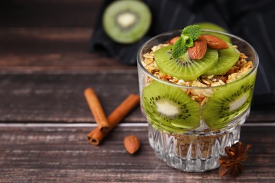 Delicious dessert with kiwi, muesli and almonds on wooden table, closeup. Space for text