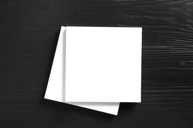 Photo of Stack of blank paper sheets for brochure on black wooden background, top view. Mock up