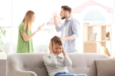 Photo of Little unhappy boy sitting on sofa while parents arguing at home