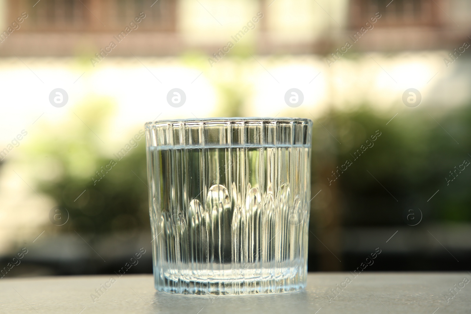 Photo of Glass of fresh water on light grey table outdoors, closeup
