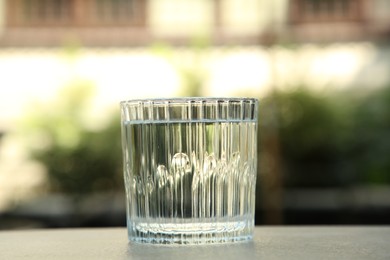 Glass of fresh water on light grey table outdoors, closeup