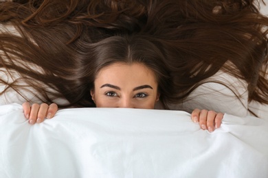 Photo of Young woman lying under blanket, top view. Bedtime