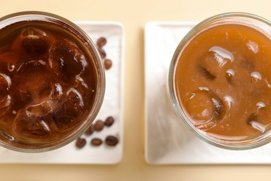 Refreshing iced coffee with milk in glasses on beige table, flat lay