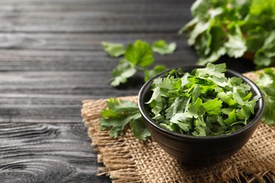 Photo of Cut fresh green cilantro in bowl on black wooden table. Space for text