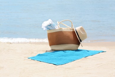 Photo of Bag with blanket, beach towel and straw hat on sandy seashore
