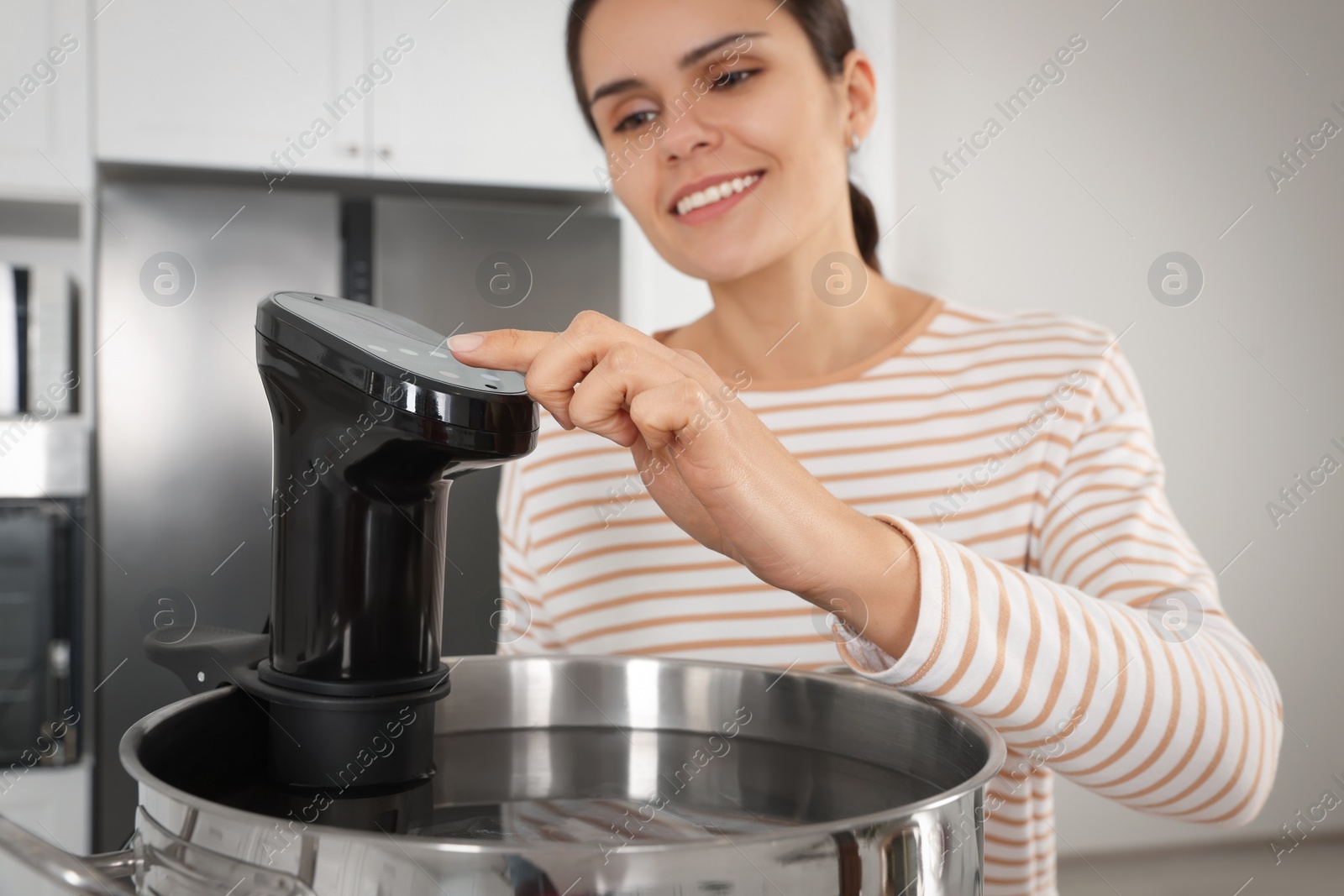 Photo of Woman using thermal immersion circulator in kitchen, focus on hand. Sous vide cooking