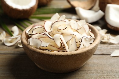Tasty coconut chips in bowl on wooden table