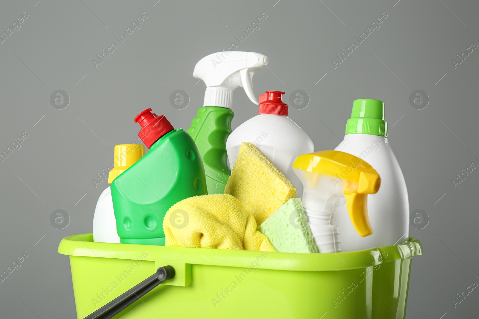 Photo of Bucket with cleaning products and tools on grey background, closeup