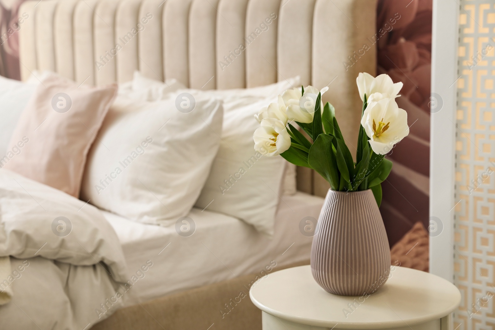 Photo of Vase with white tulips on table in bedroom. Interior element