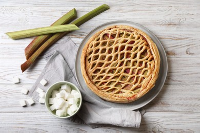 Photo of Freshly baked rhubarb pie, stalks and sugar cubes on light wooden table, flat lay