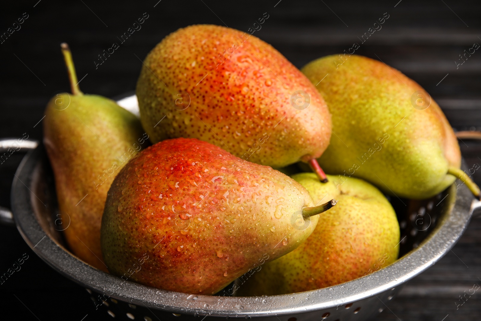 Photo of Colander with ripe juicy pears on dark table, closeup