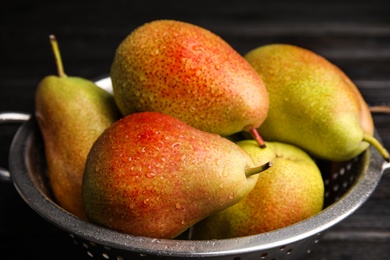 Colander with ripe juicy pears on dark table, closeup