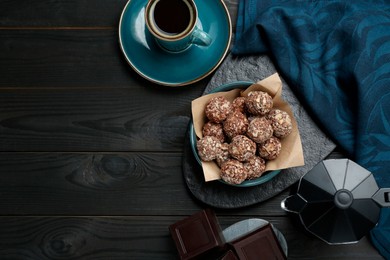 Photo of Delicious sweet chocolate candies, bars and coffee on black wooden table, flat lay. Space for text