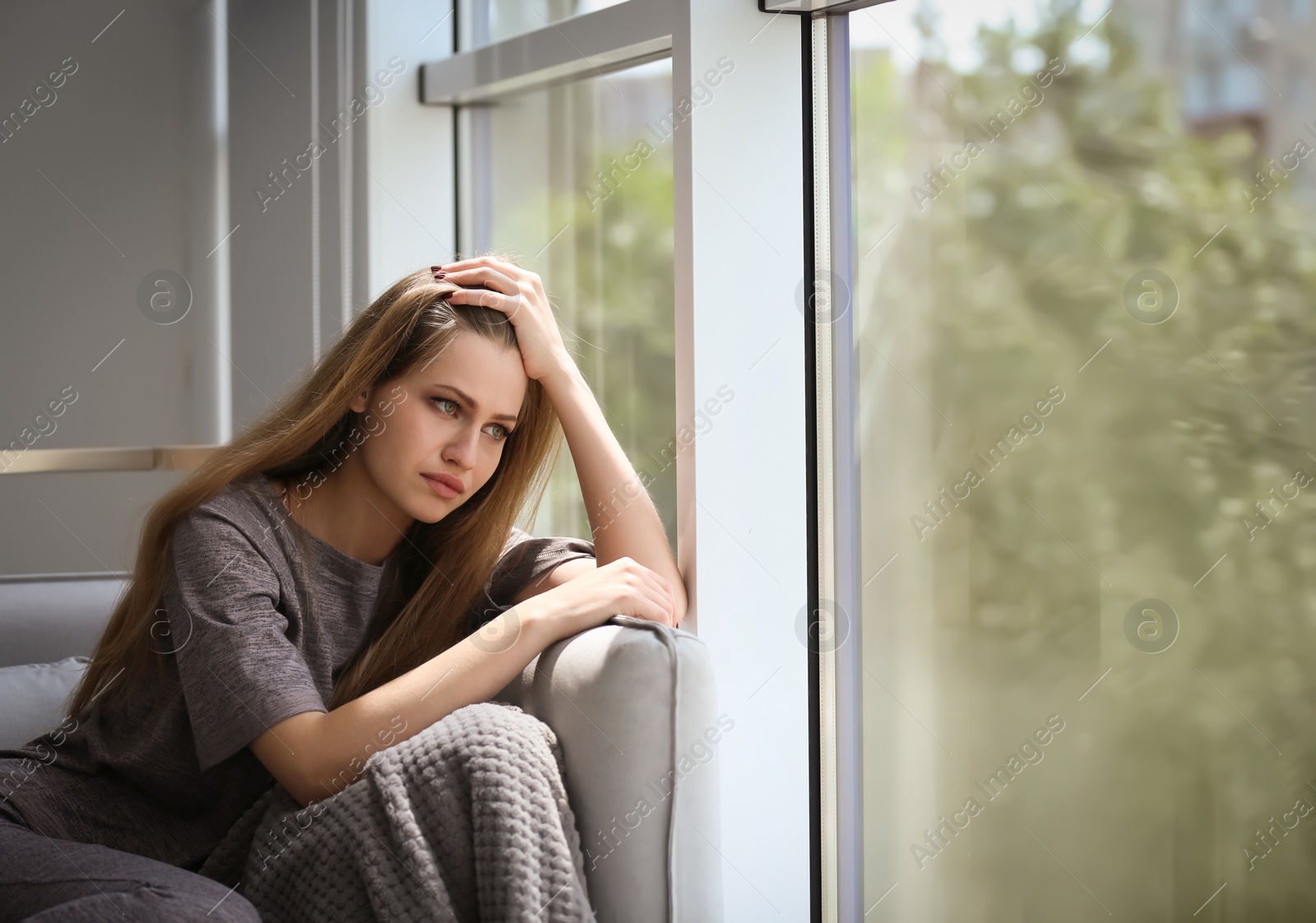 Photo of Depressed young woman sitting on sofa at home