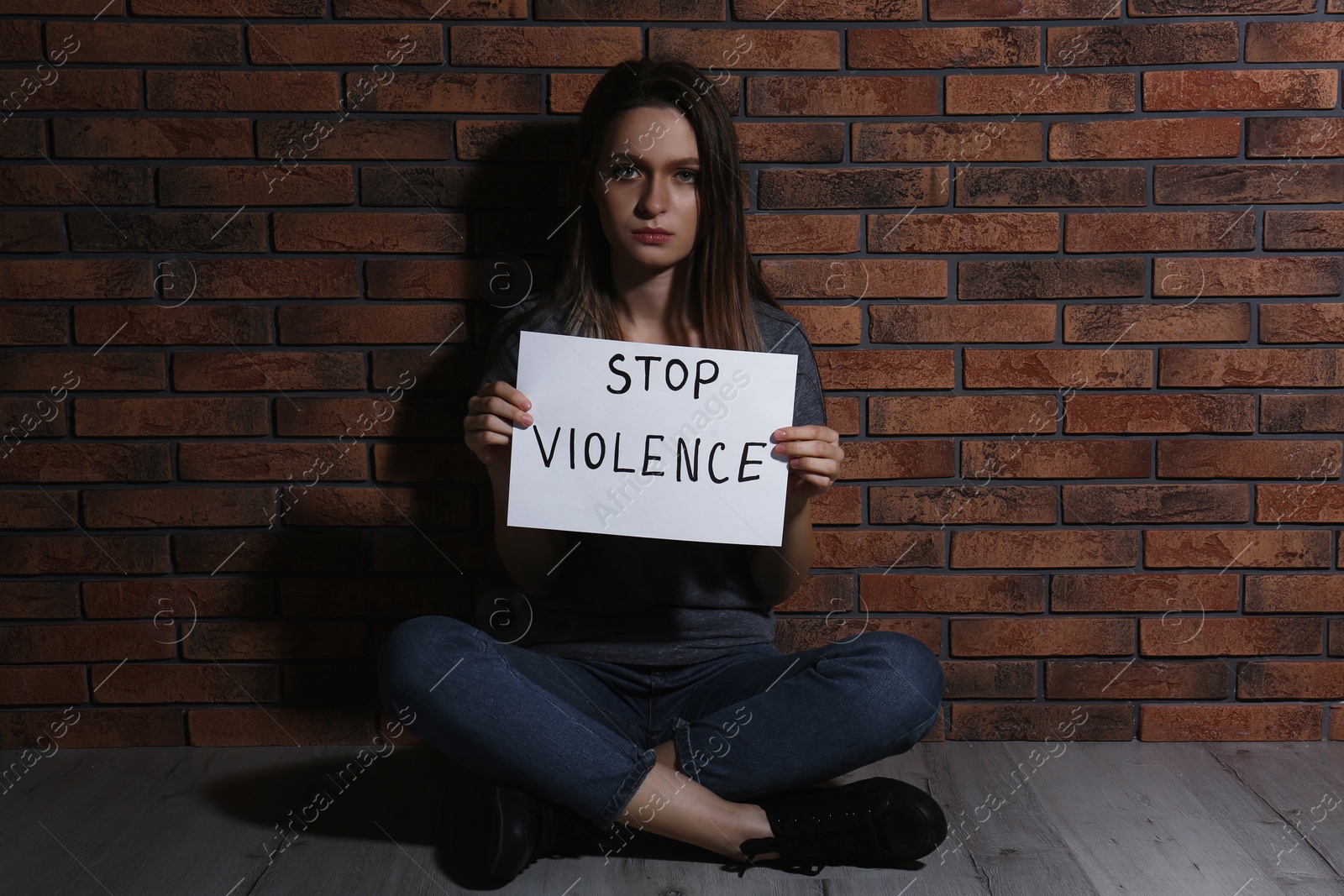 Photo of Abused young woman with sign STOP VIOLENCE near brick wall