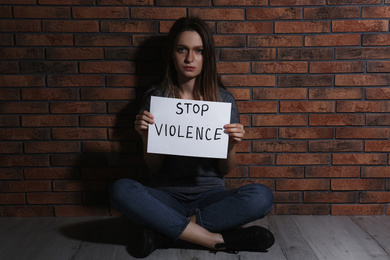 Abused young woman with sign STOP VIOLENCE near brick wall