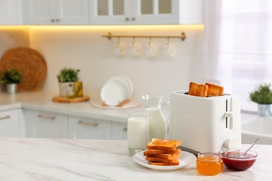 Photo of Making toasts for breakfast. Appliance, crunchy bread, honey, jam and milk on white marble table in kitchen. Space for text