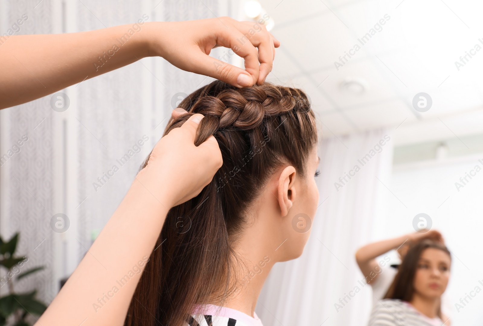 Photo of Professional stylist braiding client's hair in salon