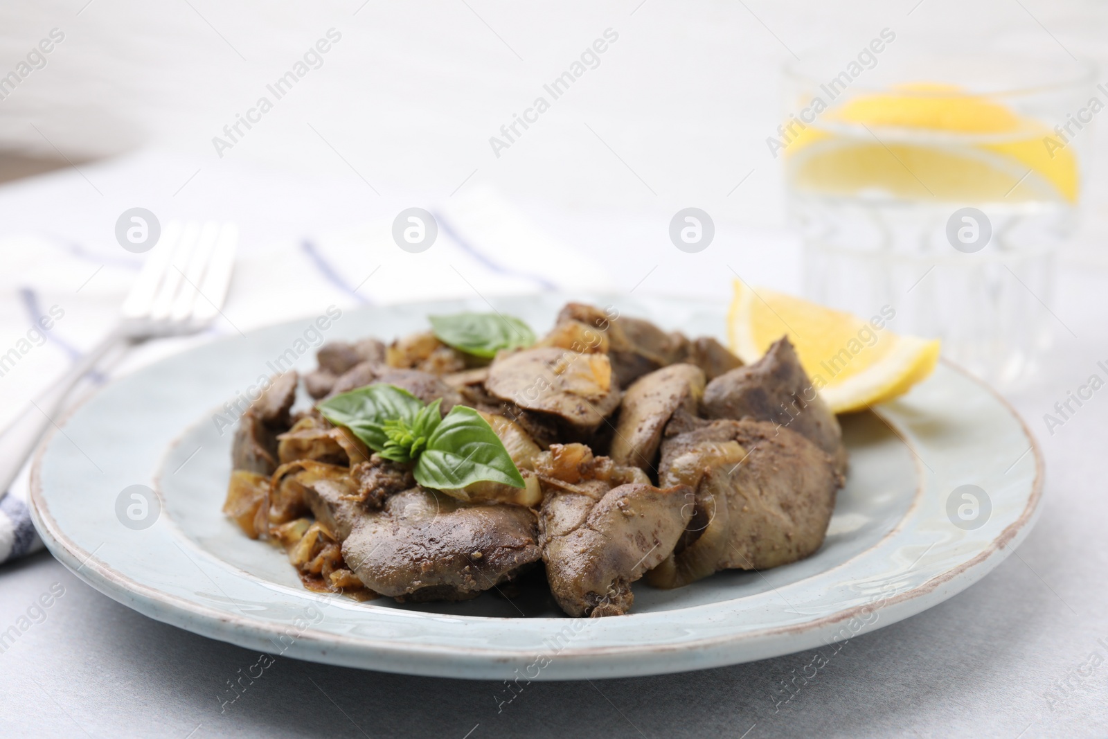 Photo of Delicious fried chicken liver with onion and basil on light table, closeup