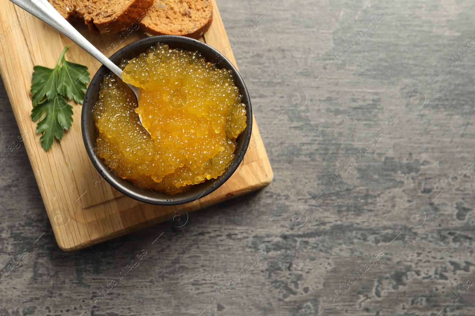 Photo of Fresh pike caviar in bowl, parsley and bread on grey table, top view. Space for text