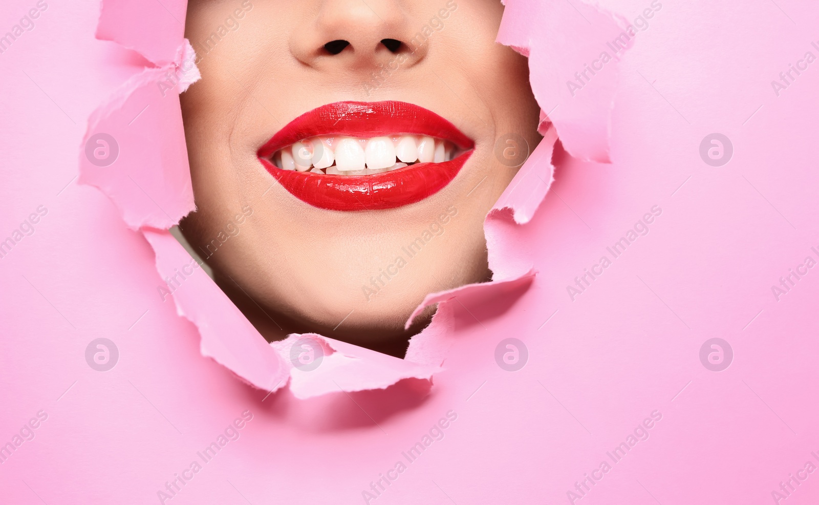 Photo of View of beautiful young woman with red lips through hole in color paper, closeup