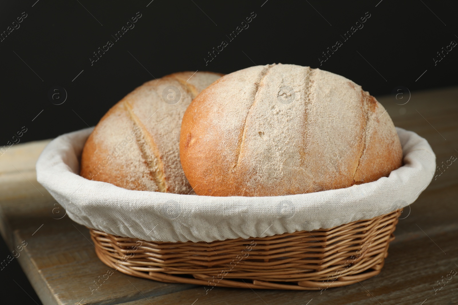 Photo of Wicker basket with fresh bread on wooden table, closeup