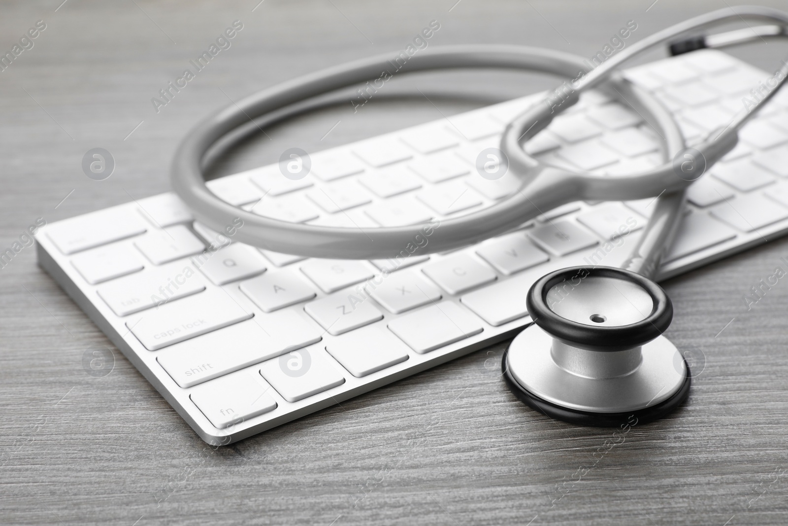 Photo of Computer keyboard with stethoscope on wooden table, closeup